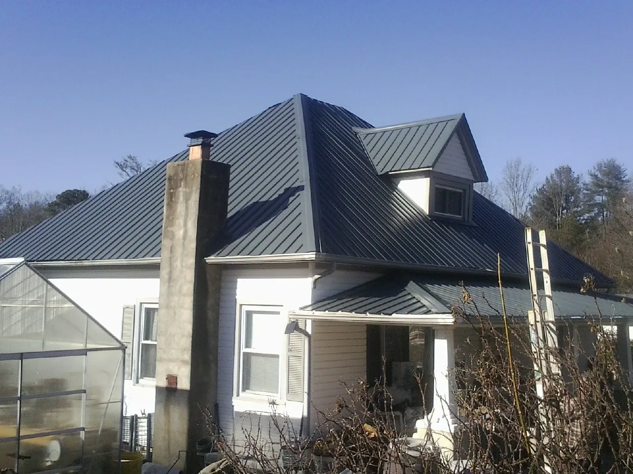 Dark blue standing seam metal roof on a white farmhouse with dormer — Slate & Tile Roof Repair by Roofing Brothers in Braxton