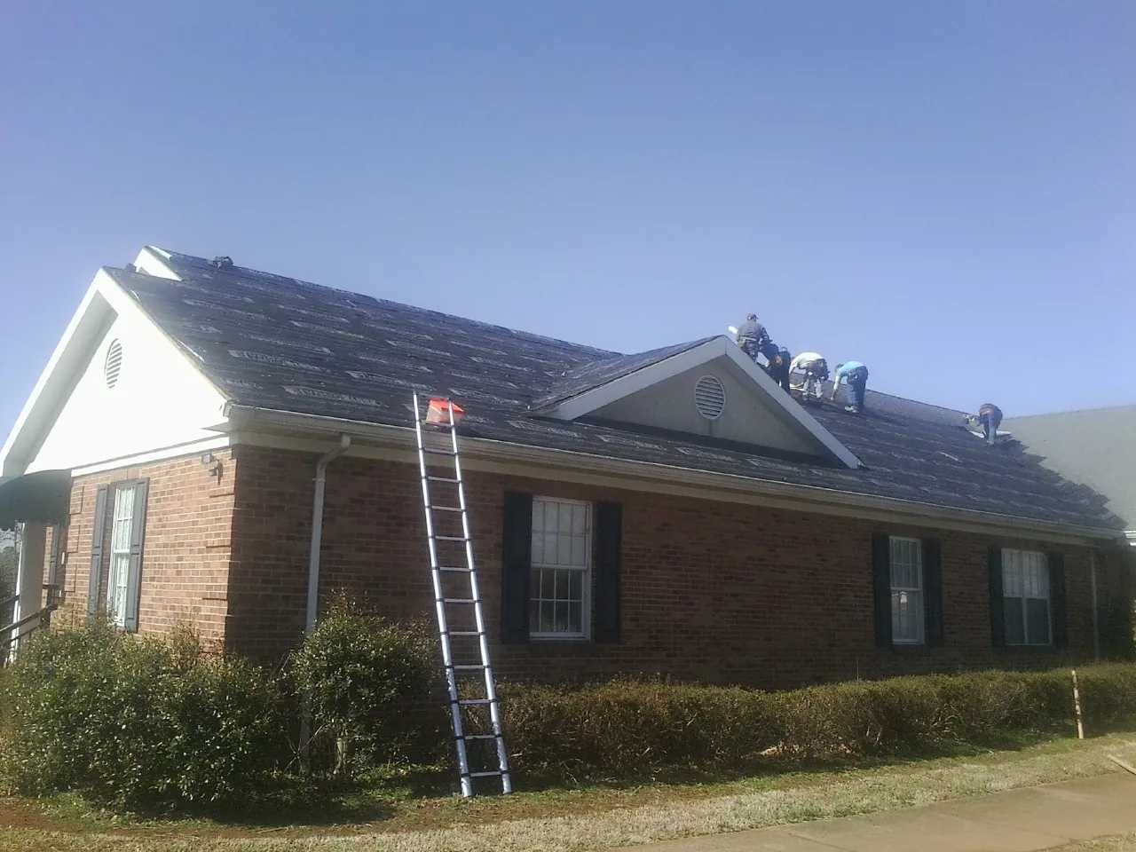 Crew tearing shingles off a brick ranch roof with a ladder set — Emergency Roof Repair work by our crew in Braxton