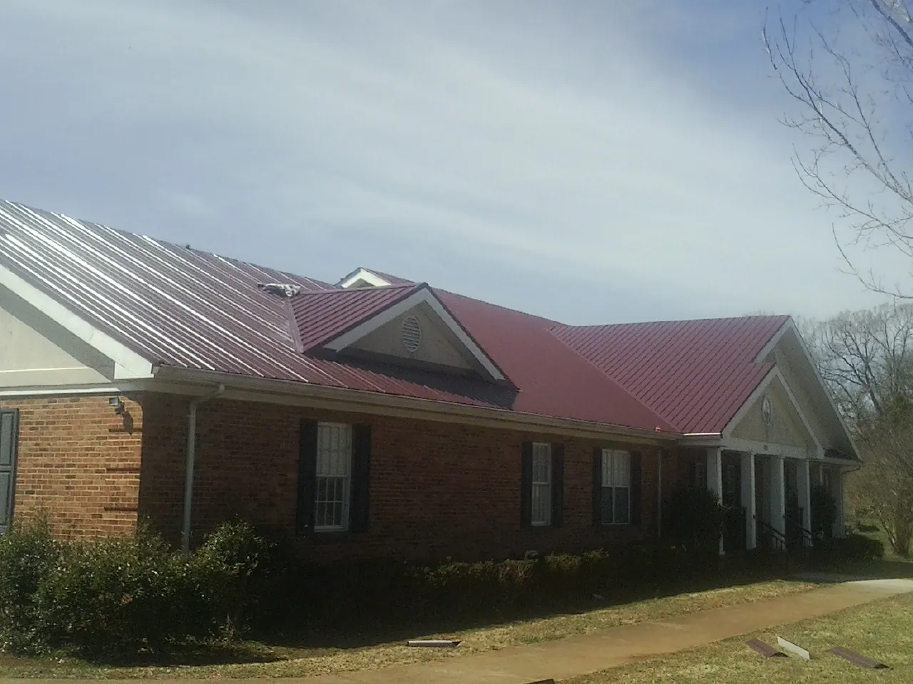 Red metal roof with gabled entries on a long brick building, from a Hail Damage Roof Repair job in Braxton