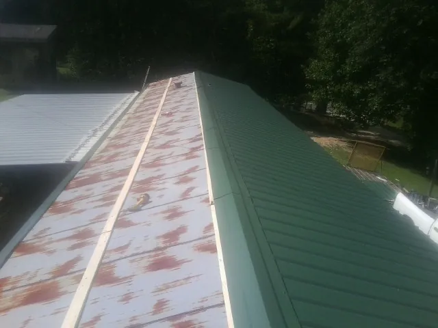 Old rusted panels beside newly installed green metal roofing — Wind Damage Roof Repair by Roofing Brothers in Braxton