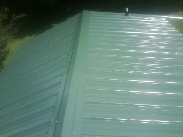 New green metal panels meeting at the ridge of a roof — Flat Roof Repair work by our crew in Braxton