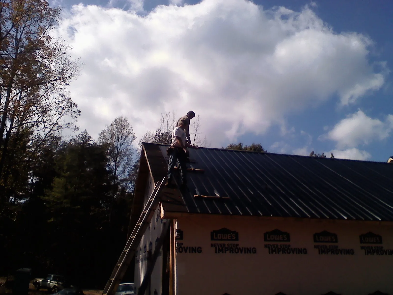 Roofer fastening dark metal panels high against a cloudy sky, from a Roof Inspection job in Braxton