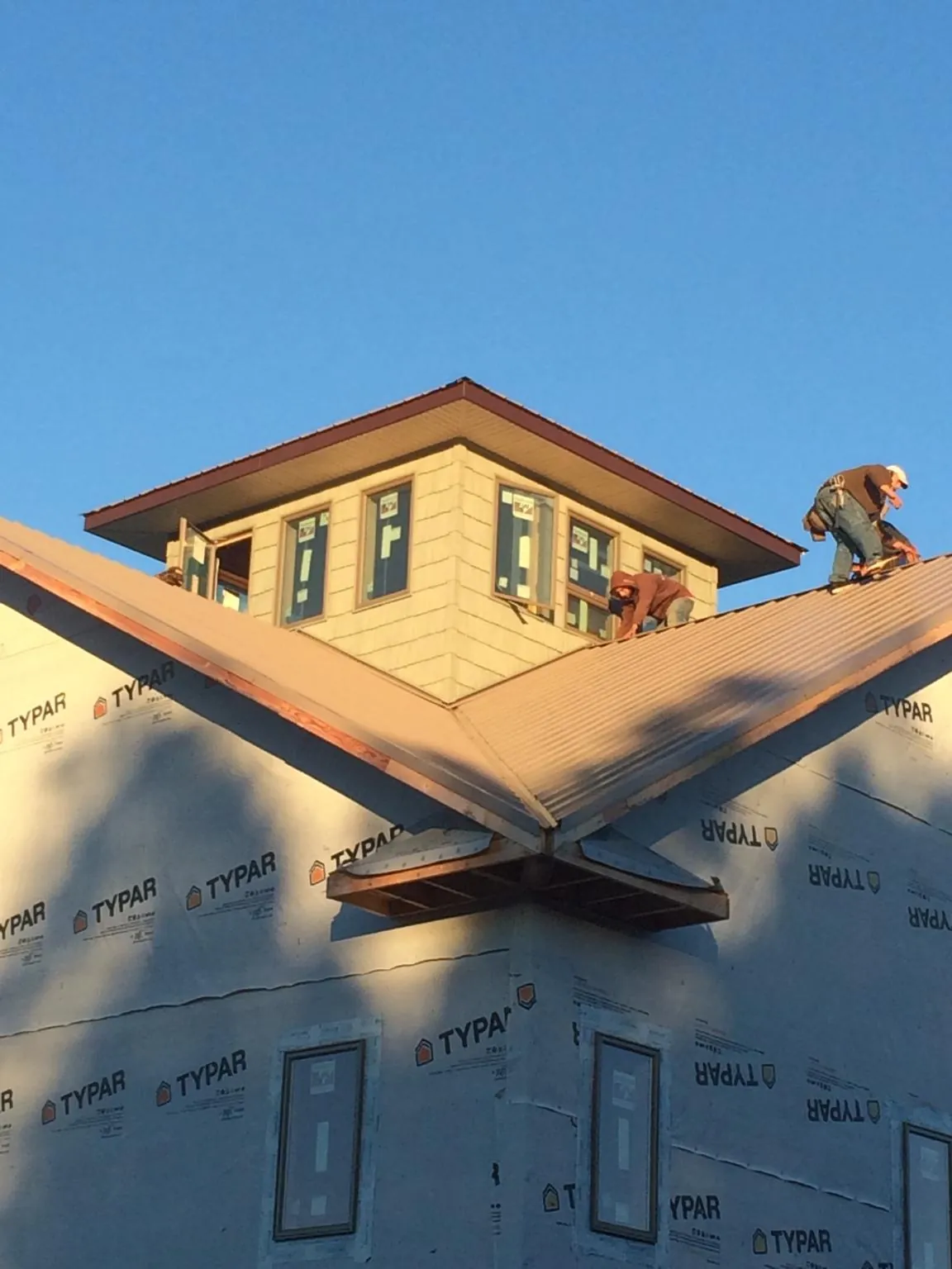 Roofers working around a rooftop cupola on a new metal roof at sunset — Roof Waterproofing in Braxton by Roofing Brothers
